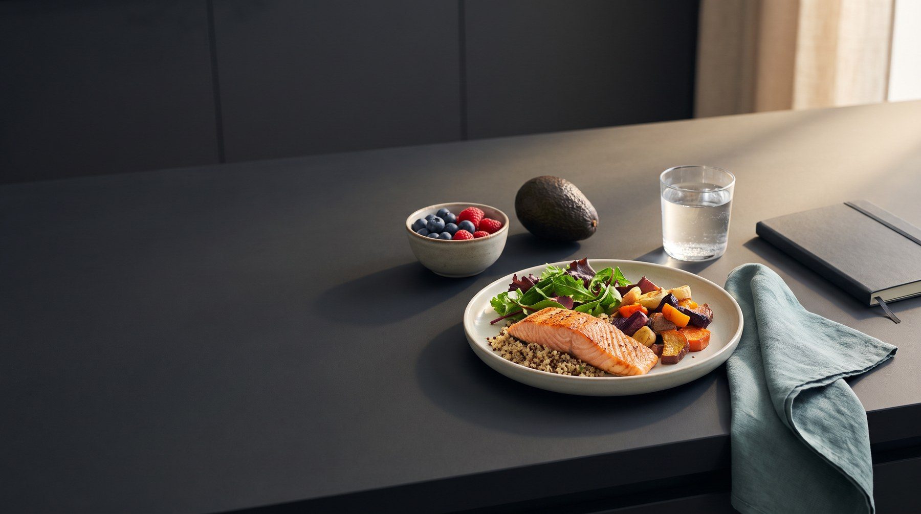 Illustrative nutrition still life with grilled salmon, quinoa, vegetables, berries and water on a charcoal surface