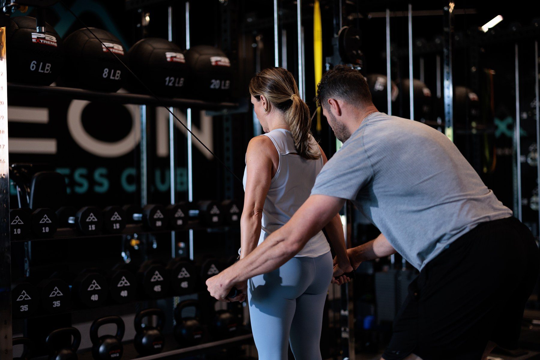 A coach guiding a member through a strength exercise inside a private training pod at Aeon Wellness Club